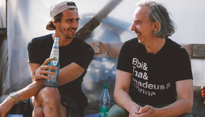 Fynn Kliemann mit umgedrehtem Cap und Olli Schulz mit gräulichen haaren sitzen lachend nebeneinander