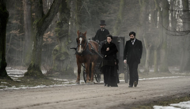 Foto zu "Freud". Auf einer nebligen Straße fährt ein Kutscher mit Zylinderhut, daneben laufen eine Frau und ein Mann.