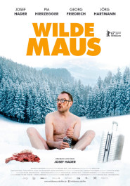 Filmplakat zu "Wilde Maus". Ein Mann um die 50, mit runder Brille und leicht geöffneten Mund, sitzt, ohne Oberteil und mit nackten Beinen im Schnee vor einem verschneiten Wald.