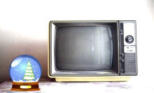 Ein alter Fernseher mit einem Holzrahmn neben einer Weihnachts-Schneekugel mit Tannenbaum.