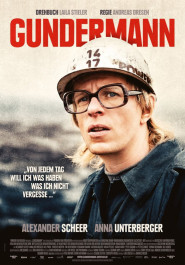 Filmplakat zu "Gundermann". Ein junger Mann mit blonden Haaren, Bauhelm, schwarzer Brille und leicht geöffnetem Mund.