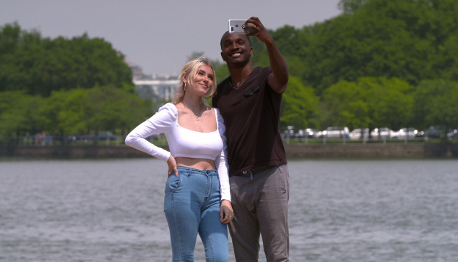 Eine junge weiße Frau mit blonden Haaren und ein junger schwarzer Mann posieren für ein Selfie vor dem Kapitol in Washington D.C.