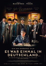 Filmplakat zu "Es war einmal in Deutschland". Sechs Männer in Anzügen und mit Krempen-Hüten, vor ihnen sitzend eine Frau in Uniform